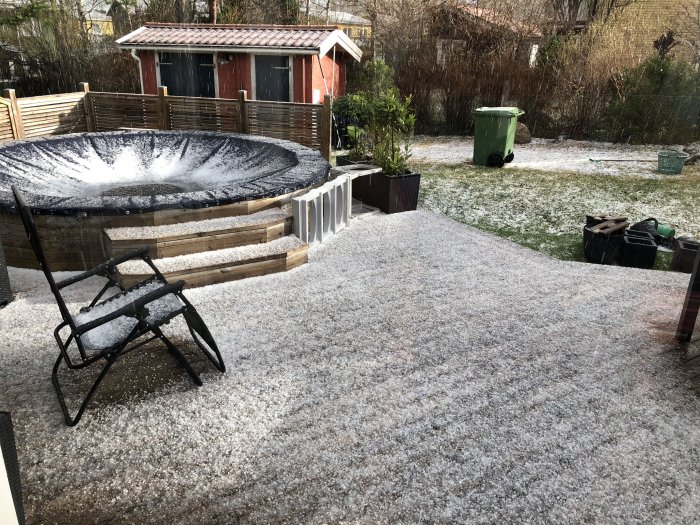 Trädgård med trampolin och möbler täckt av hagel, ironisk kontrast till sommarkänsla.