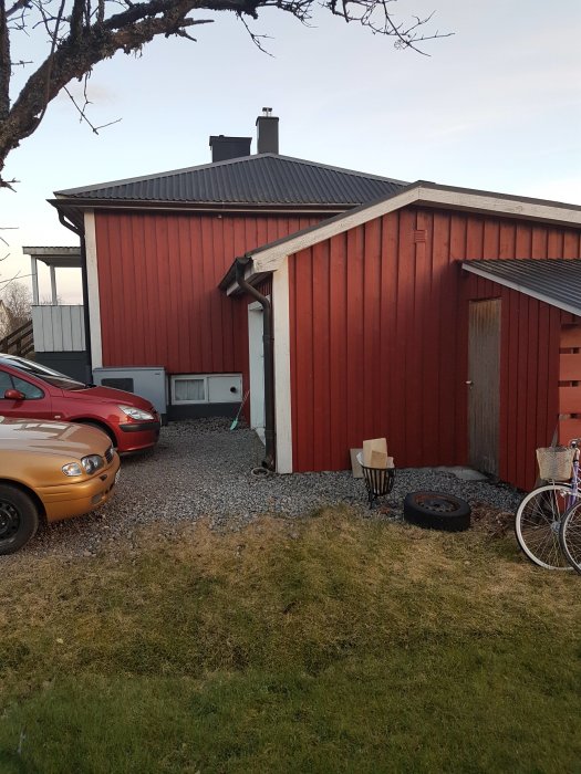 Rödmålat trähus med källaringång och nivåskillnad på gräsmattan, potentiell utbyggnadsplats.