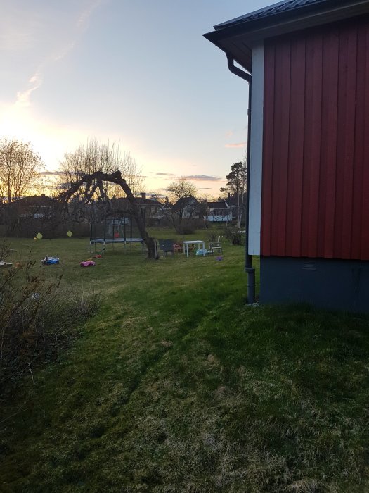 Rödmålad husgavel med gräsmatta och liten nivåskillnad, möjlig utbyggnadsplats för hem.