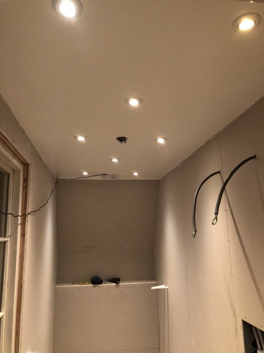 Nyligen installerade downlights i ett oinrett badrumstak med synliga kabeldragningar och verktyg på en hylla.