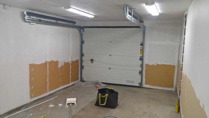 Nyrenoverat garage med nymålade vita väggar och stängd port, målarverktyg och skyddsplast på golvet.