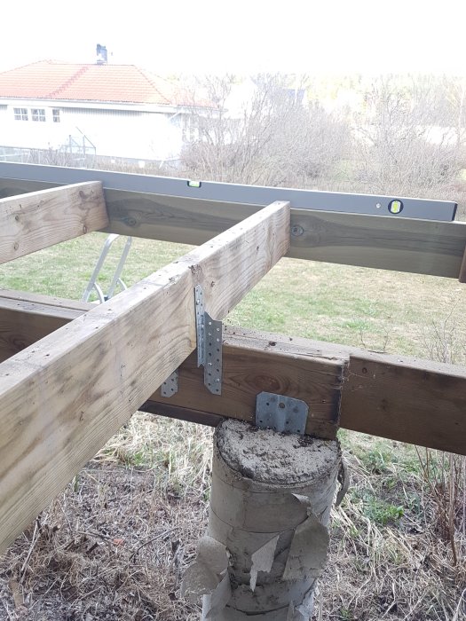 Altan under ombyggnation med ny regel fäst vid befintliga träbjälkar och plint, visar vattenpass för korrekt nivåering.