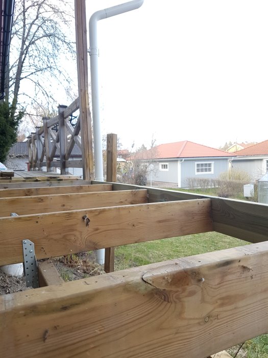 Uppbyggnad av ett uterumsgolv med nya och gamla träreglar, vissa ojämna, med synlig stödkonsol och bakgrund av bostadshus.