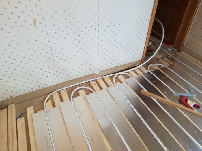 Installationsprocess för golvvärme med glespanel och slingor på ett underkonstruktionsgolv under renovering.