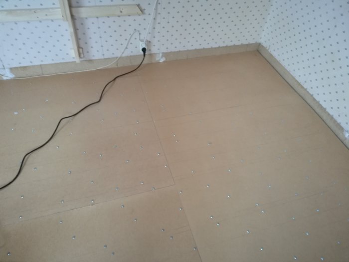 Delvis installerat golv med mineralull under hård board och synliga montageskruvhuvuden.