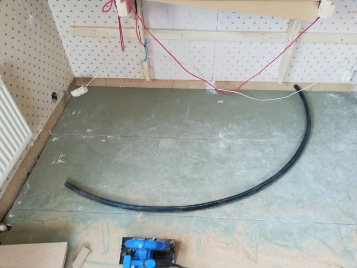 En renoveringsbild som visar golvvärmeslangar ovanpå 22mm golvspån i ett pågående byggprojekt med verktyg synliga.