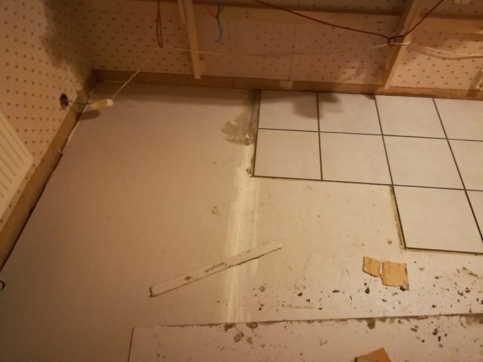 Pågående golvrenovering med delvis lagt kakelgolv intill en oklädd vägg, skivmaterial och verktyg syns.