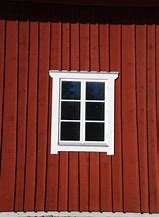 Rödmålad kilsågad träpanel med varierad bredd runt ett vitmålat fönster.