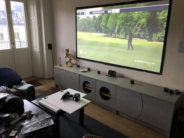 Vardagsrum med nyinstallerade dörrar på TV-överskåp, golf på TV:n och verktyg på bordet.