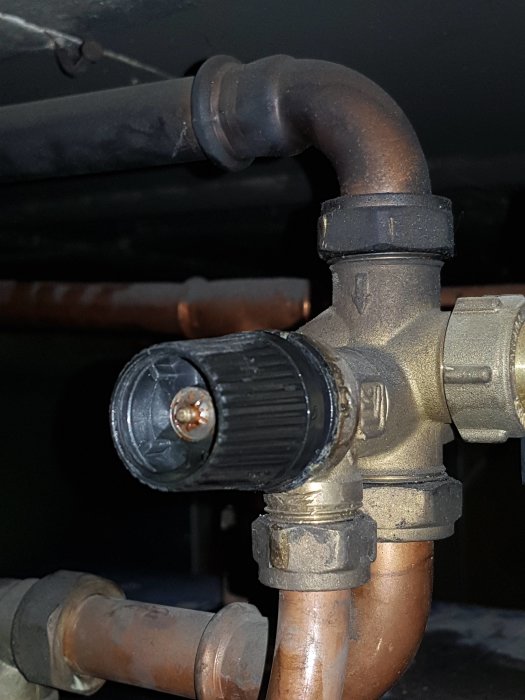 Rörkoppling med svart ventilhjul på en vedpanna, som söker ersättning.