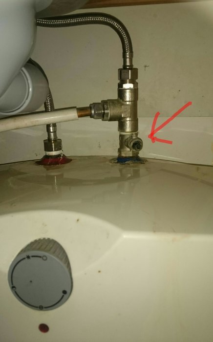 Läckande ventil under vask med vattenpöl, röd pil pekar på droppande del.