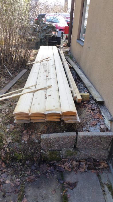 Stapel av vitmålad stockpanel liggandes bredvid en husvägg, redo att bortskänkes.