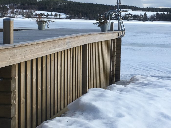 Träbrygga med snö omgivet av en frusen sjö, med synliga sättningar på bryggans yta.