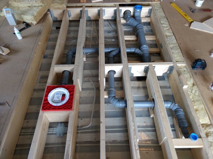 Installation av avloppsrör i träreglar på en byggarbetsplats före isolering och golvläggning.
