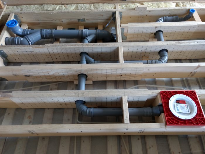 Avloppsrör av plast installerade mellan träbjälkar i ett hus under konstruktion, redo för isolering och golvspån.