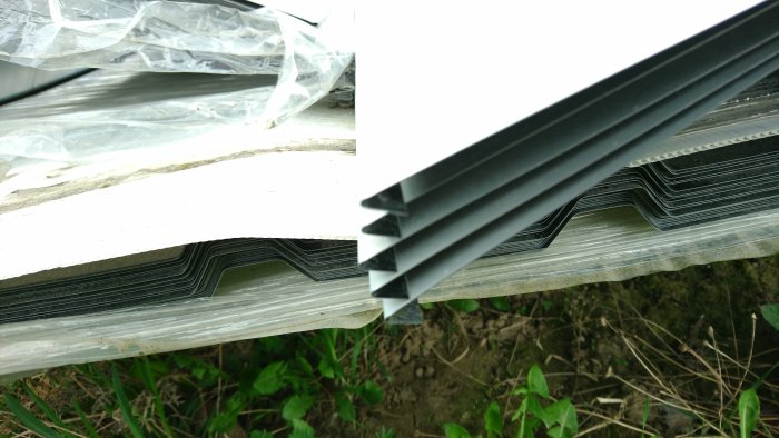 alt="Svarta plåttakskivor för 18R och ränndal med uppvik staplade utomhus