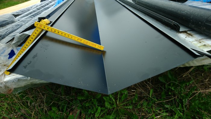 Svart plåttak och ränndal uppmätta med tumstock på gräs.