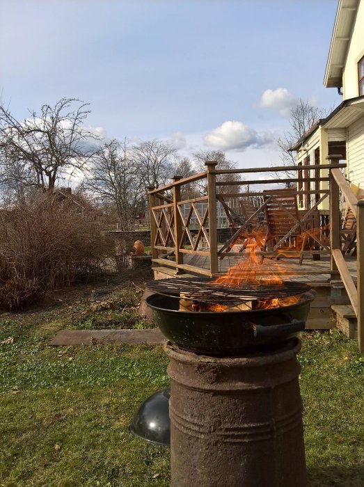 Eld flammar upp ur en rostig trumma omvandlad till en grill på en bakgård med en träveranda i bakgrunden.