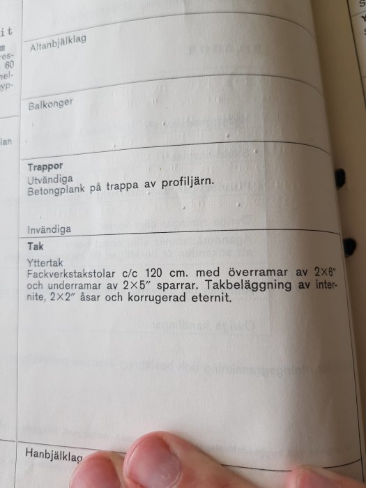 Hand som håller en sida i en handbok om byggkonstruktion, visande text om yttertakspecifikationer.