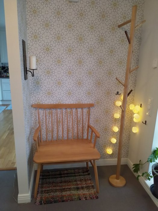 Hemgjord klädhängare i trä bredvid en matchande pinnsoffa, mot en tapetserad vägg med blommönster.
