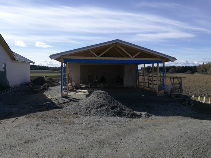 Nybyggt vädertätt garage med carport i konstruktion mot en klar himmel.