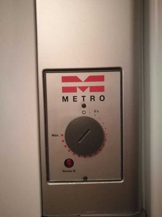 Termostat för värme med METRO-logotyp, inställningsratt och indikatorlampa för 'varme til'.