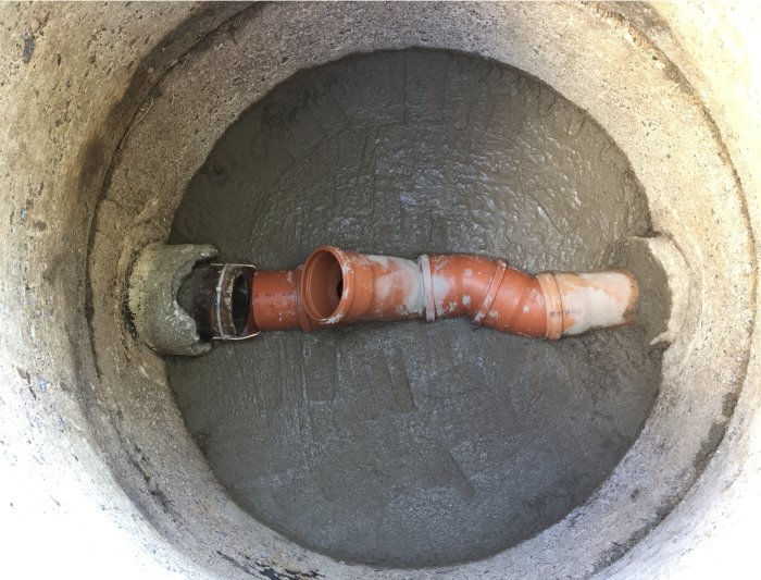 Brunn med betongbotten och anslutet orange avloppsrör, inget vatten synligt.