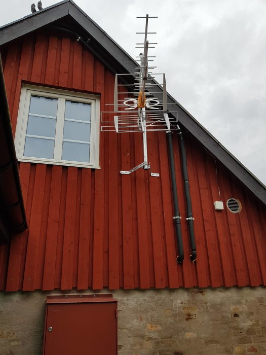 En ny tv-antenn installerad på en röd husvägg med fönster, under en grå himmel.