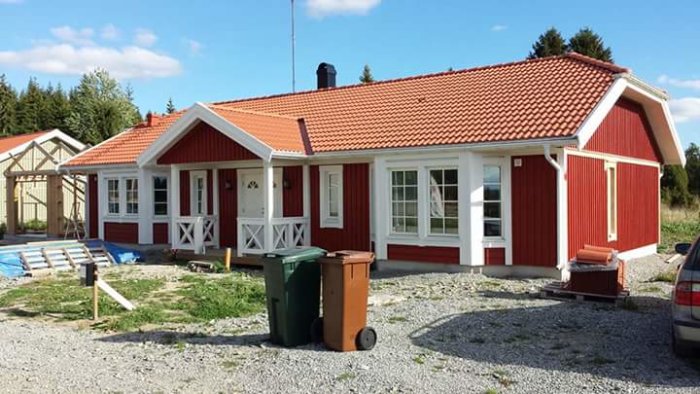 Enplans rött hus med vita knutar och brutet tak, byggarbetsplats i förgrunden.