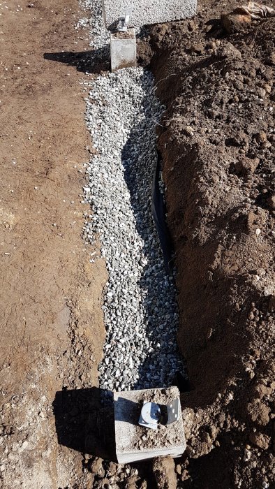 Grävd ränna med makadam på geoduk och lecablock vid sidan, förberedelser för byggprojekt.