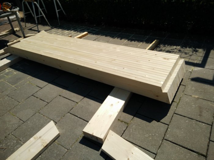 Sågade takstolar i trä redo för montering på stenlagd mark utomhus.