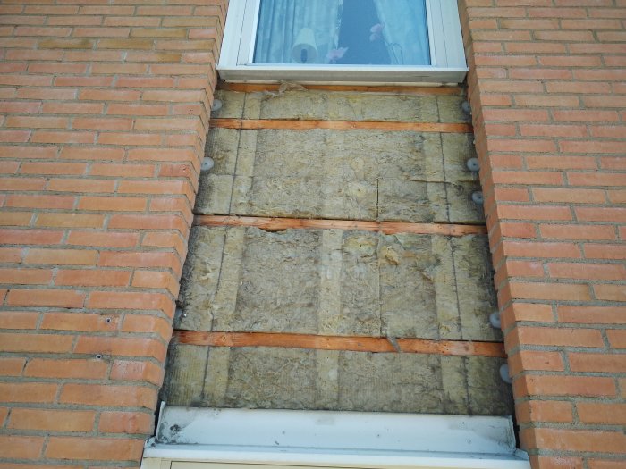 Väggparti där tegelstenar är borttagna exponerar isolering och träreglar för renovering.