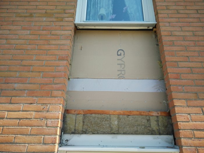 Delvis demonterad vägg under fönster med exponerad isolering och träbjälkar för renovering.