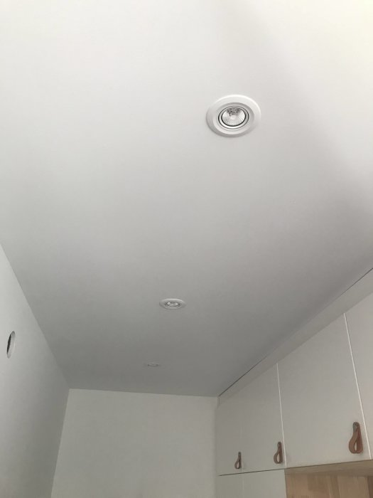 Nyinstallerade infällda spotlights i ett vitmålat tak över vita köksskåp med trähandtag.
