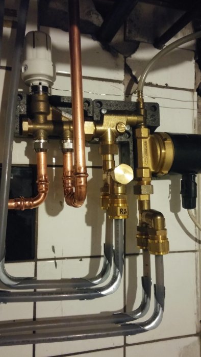 VVS-installation med kopparledningar och en svart pump, mot en vägg med synliga tegelstenar.