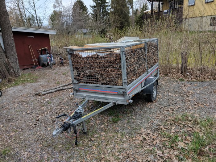 Släpvagn full av löv och grenar parkerad utomhus, redo för tömning vid en återvinningscentral.