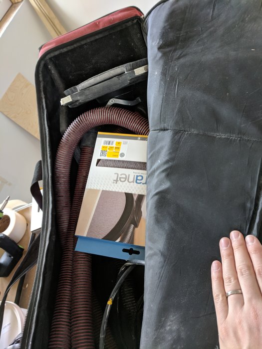 Öppen verktygsväska med spackelverktyg och en förpackning Mirka Abranet slipnät, vid sidan av en hand.