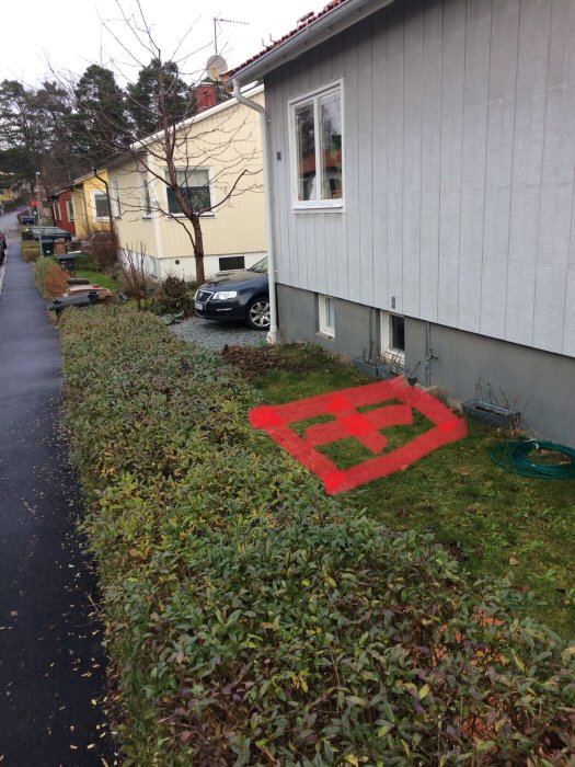 En del av ett hus och trädgård med en uppmärkt röd rektangel på marken, markerande grävningsområde.