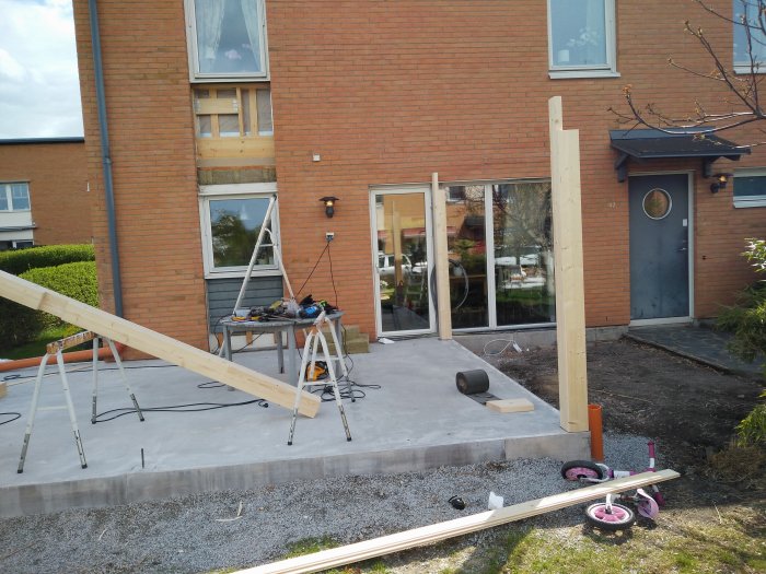 Utbyggnadsprojekt på en tegelvilla, med träreglar och byggverktyg på en nygjuten betongplatta.