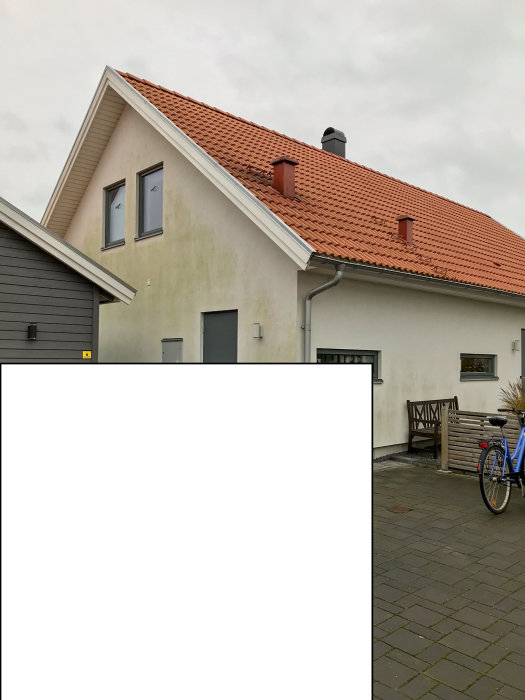 Ett nybyggt hus med putsad fasad i vitt, rött taktegel, och en cykel framför.