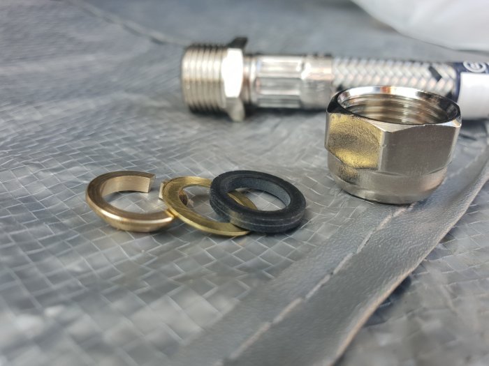 Koppling för köksblandarslang med konisk klämring, gummi- och mässingspackning omonterad på grå yta.
