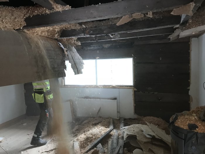 Person i arbetskläder rivstartar renovering av rum med isoleringsmaterial som faller ner.