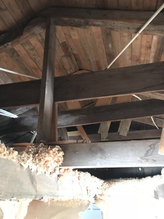 Takbjälkar och isolering i ett pågående byggprojekt med synligt trätak och elektriska ledningar.