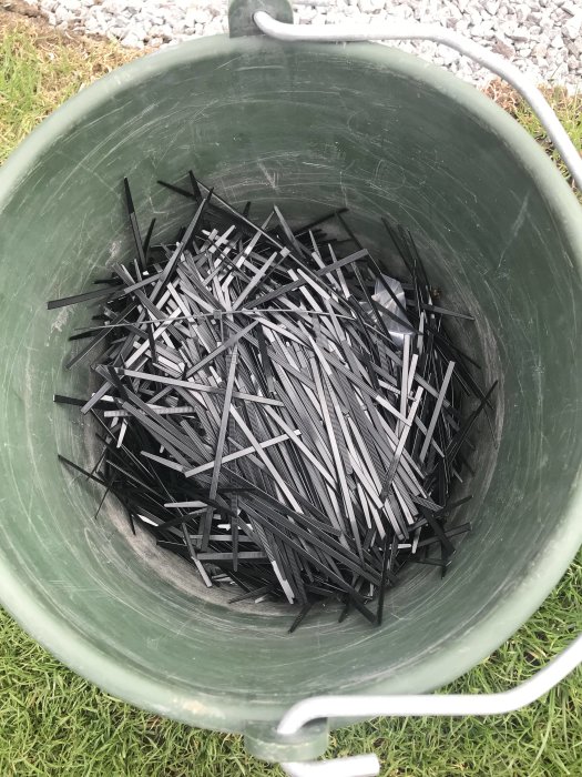 En hink fylld med svarta buntband på en gräsmatta.