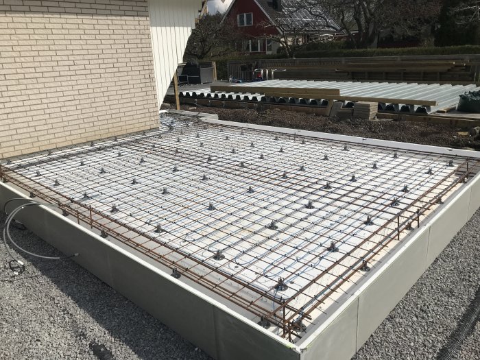 Installation av golvvärme med armeringsjärn och buntband på en byggplats, med tomslangar och byggnader i bakgrunden.
