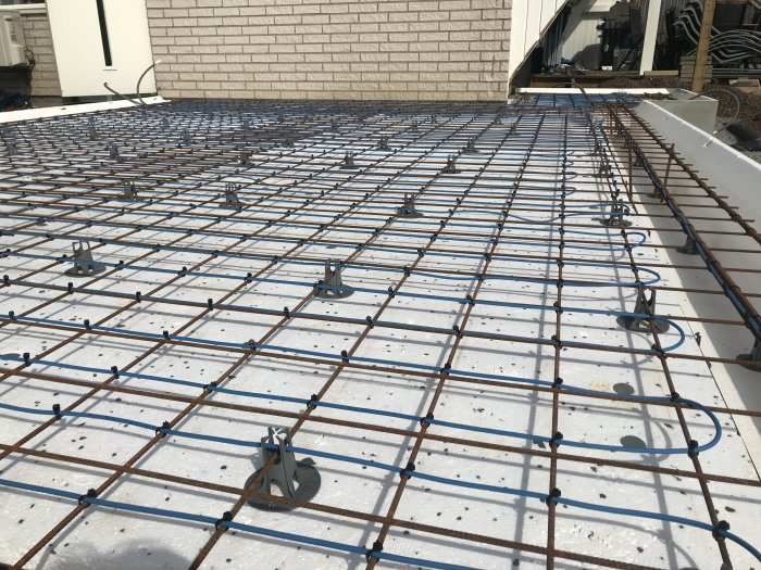 Installation av golvvärme med värmeslingor fästa vid armeringsnät, tomslangar dragna vid sidan.