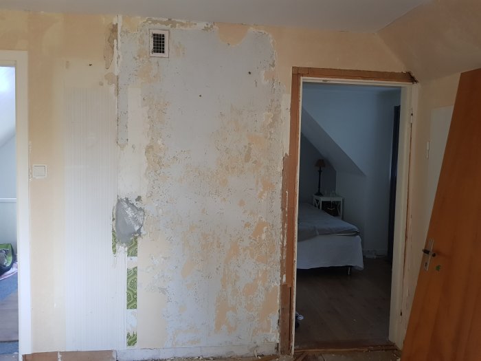 Renoveringsbehov av en skadad och flagnande innervägg med synlig gips och tapetrester.