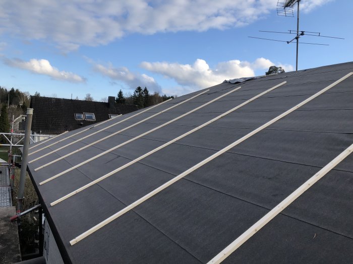 Tak med ojämnt liggande svart takpapp under konstruktion av träribbor, med klar himmel i bakgrunden.