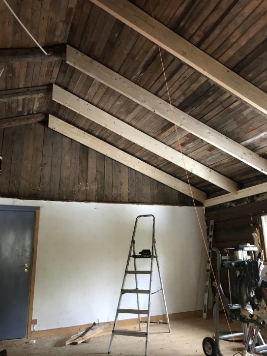 Renovering av interiör med synliga takbjälkar och stege, möjlig plats för kamin/skorsten.