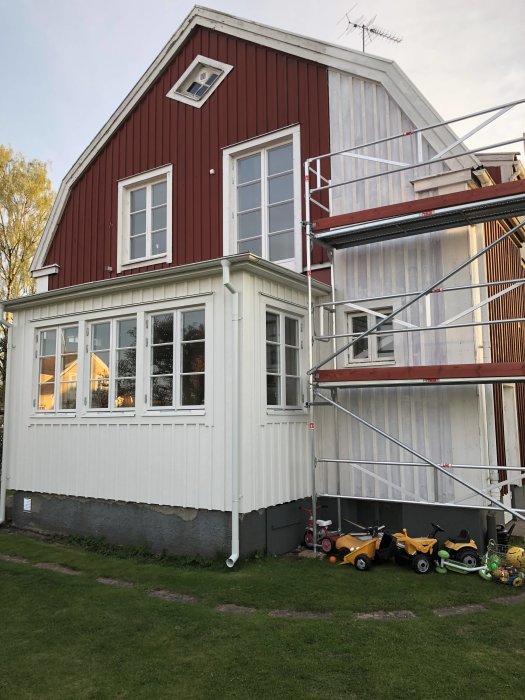 Renovering av hus med röd träpanel och ställning för målning, fönsterbleck synligt.